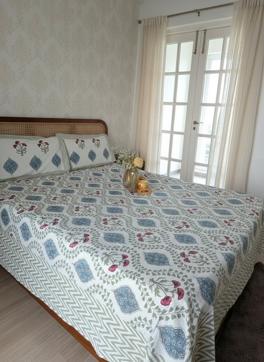 Bed with floral patterned bedsheet in a room with light-colored walls and a window.