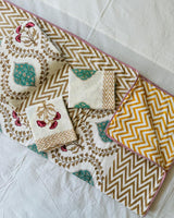 Close-up of beige gold floral vine mulmul cotton fabric with a teal medallion and red flowers