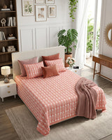 Harsingar Pink bedsheet, coral-pink ground with rows of white flowering stems, in a bedroom with rose cushions and a knit throw