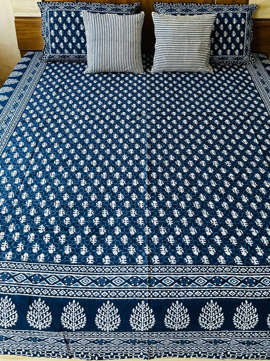 Bed with blue and white patterned bedspread and pillows in a room.