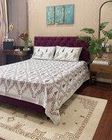 Bed with floral patterned bedspread and pillows in a room setting.