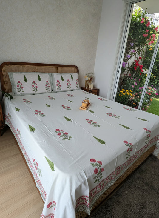 Bed with floral-patterned bedsheet in a room with a white wall and wooden floor.