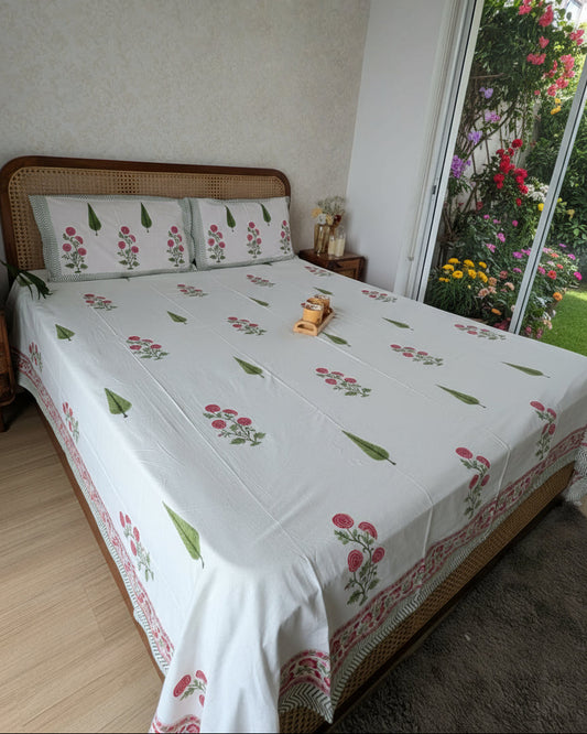 Bed with floral-patterned bedsheet in a room with a white wall and wooden floor.
