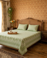 Sagar Green bedsheet, sage-green geometric maze with a medallion-flower border, on a bed with a carved cane headboard with a tea tray
