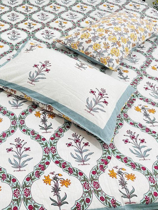 Bed with floral patterned bedsheet and 2 reversible matching pillows in blue, yellow & red