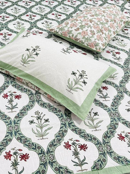 Bed with floral-patterned bedsheet and 2 reversible pillows in green and red