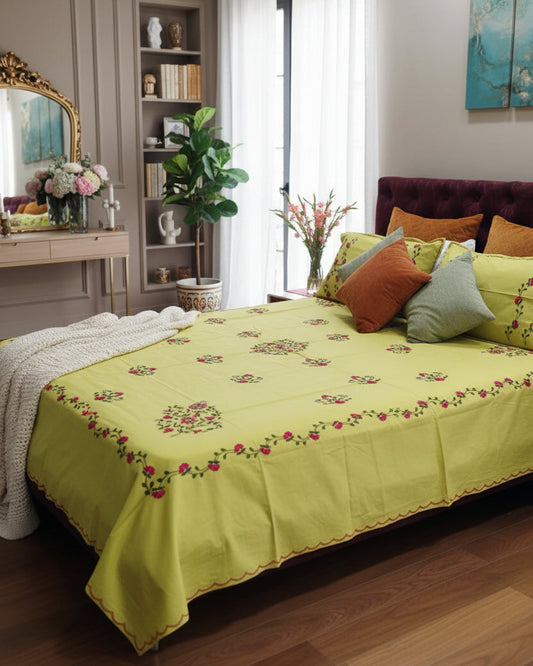 A yellow-green embroidered bedspread and matching pillowcases on a bed in a bedroom setting.