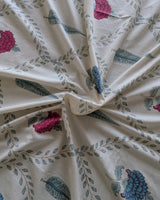 Close-up of ivory cotton fabric with a green vine trellis and pink and blue floral motifs