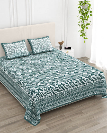 Aakriti Blue bedsheet, deep teal diamond-maze print, in a studio shot against a cream headboard