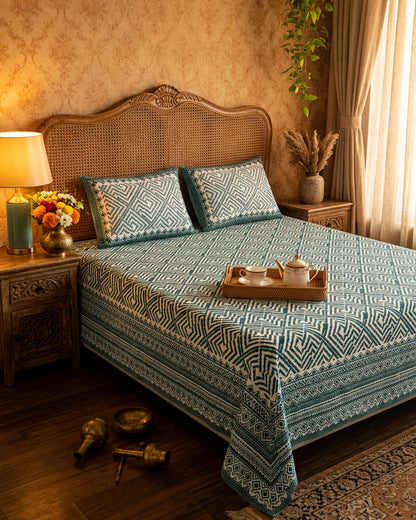 Aakriti Blue bedsheet, deep teal diamond-maze print, on a bed with a cane headboard and a tea tray