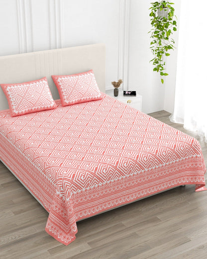 Aakriti Pink bedsheet, coral-pink diamond-maze print, in a studio shot against a cream headboard