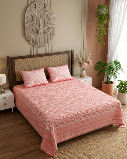 Aakriti Pink bedsheet, coral-pink diamond-maze print, on a bed with a cane headboard with macramé