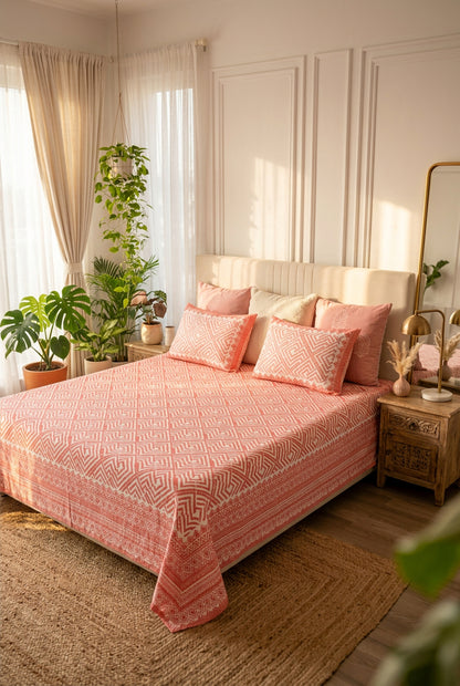 Aakriti Pink bedsheet, coral-pink diamond-maze print, on a bed with a cream headboard with blush cushions