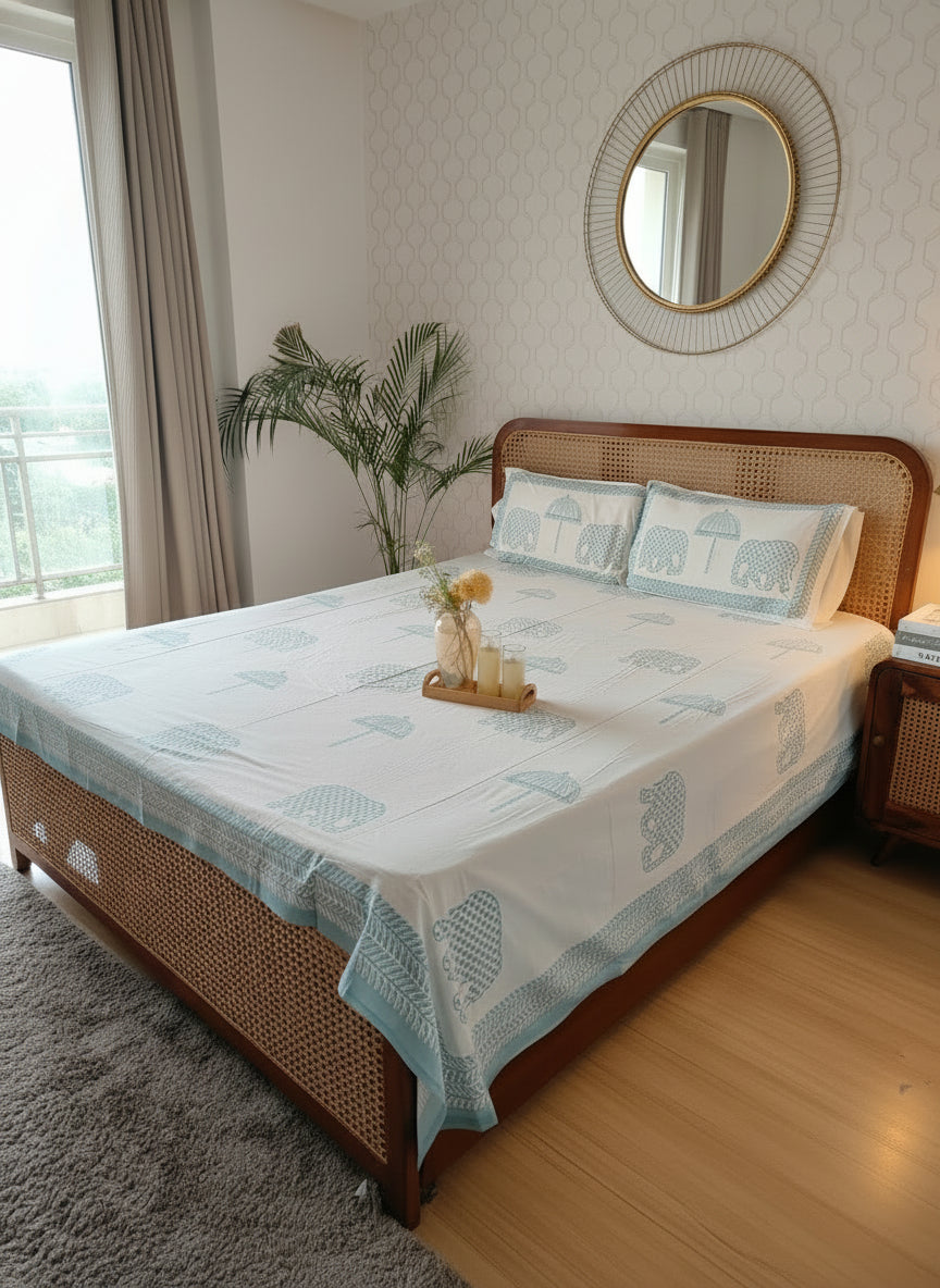 Bed with white and blue patterned bedding in a room with a plant and window.
