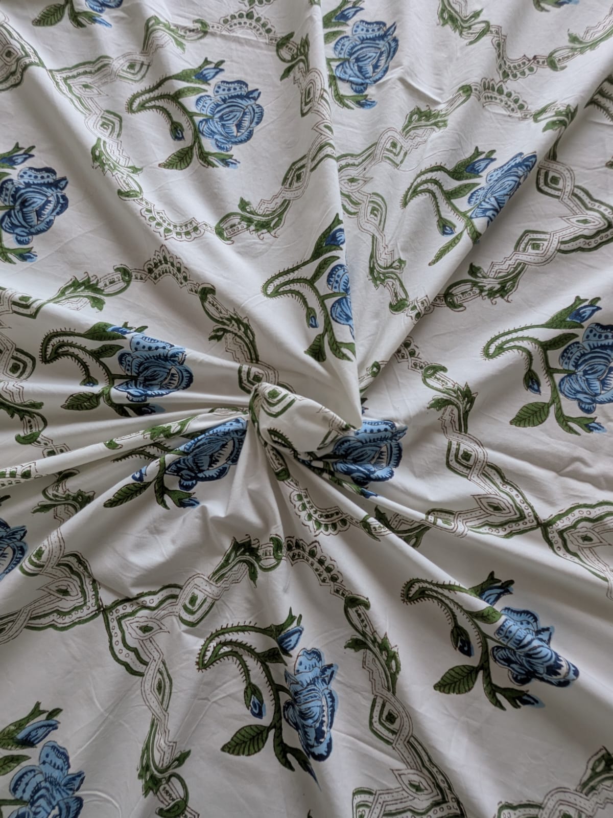 Close-up of fabric with blue floral and green leaf patterns on a white bedsheet