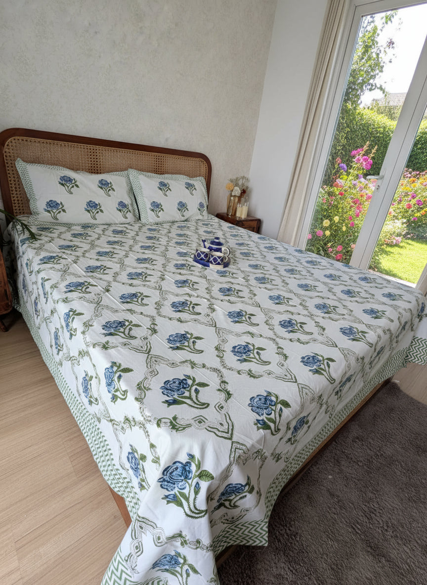 Bed with blue floral-patterned bedsheet in a room with wooden flooring and white walls