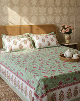 Sage green floral cotton bedsheet with pink roses on a beige upholstered bed with reversible pillow covers