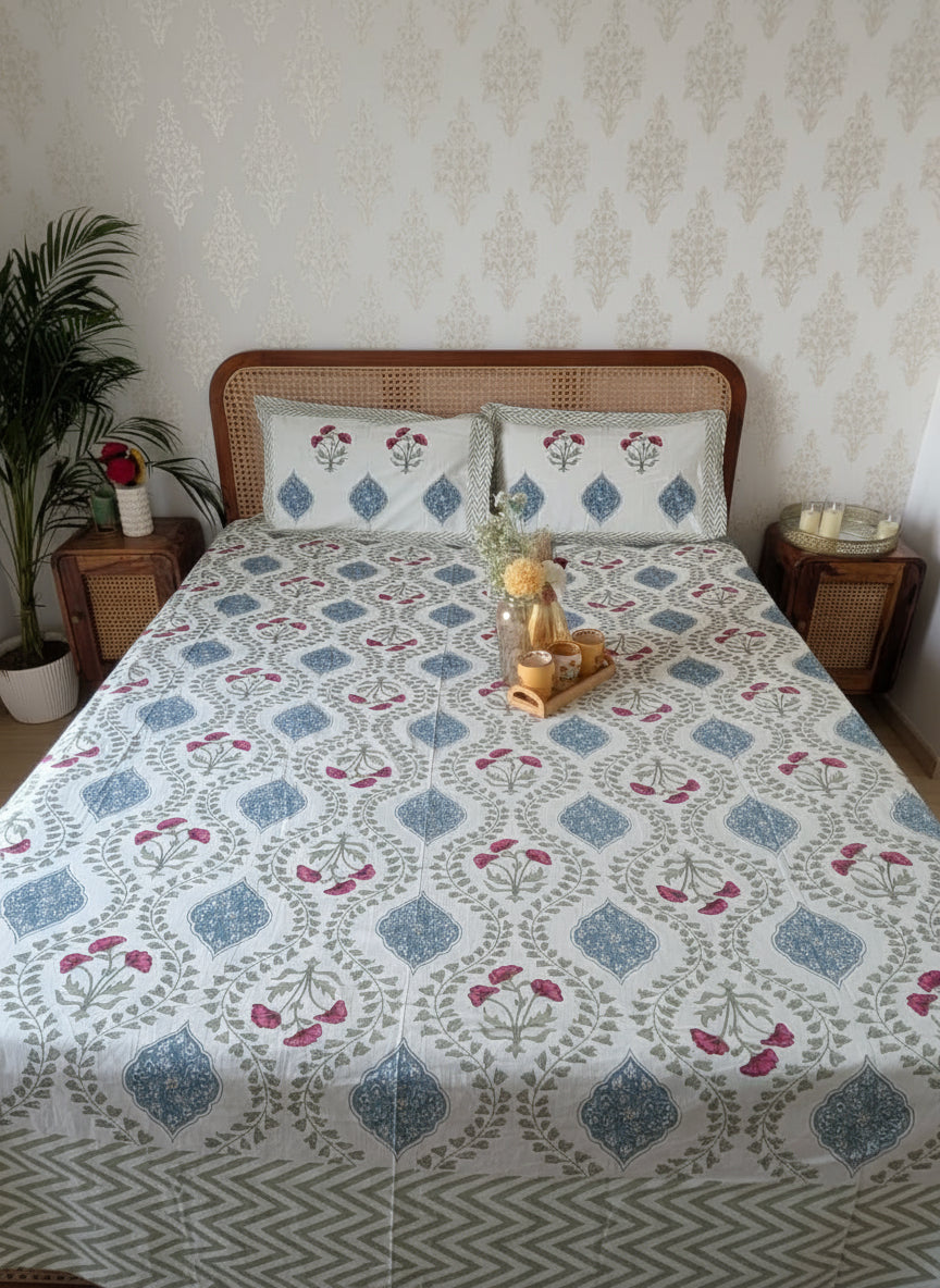 Bed with floral patterned bedsheet with 2 matching pillow covers in a room with a plant and side tables.
