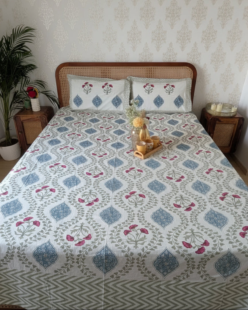 Bed with floral patterned bedsheet with 2 matching pillow covers in a room with a plant and side tables.