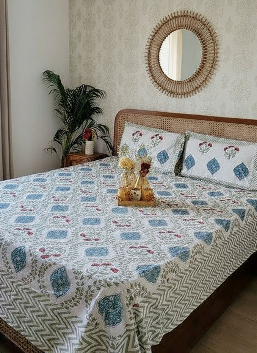 Bedroom with a bed covered in a patterned bedsheet, reversible pillows, and a small table with decor items.