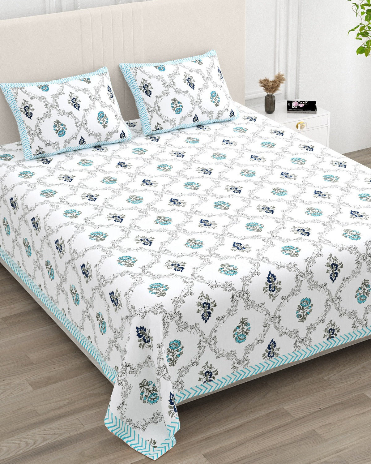 Chameli Blue bedsheet, grey trellis jaal on white with aqua bloom booti, in a studio shot against a cream headboard