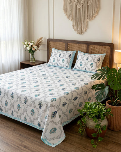 Chameli Blue bedsheet, grey trellis jaal on white with aqua bloom booti, on a bed with a cane-panel headboard with plants