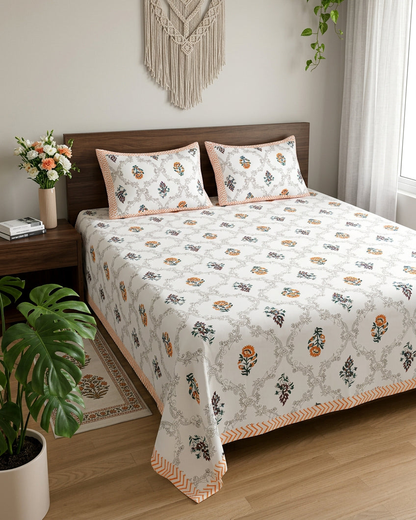 Chameli Orange bedsheet, grey trellis jaal on white with orange bloom booti, on a bed with a wood headboard with macramé