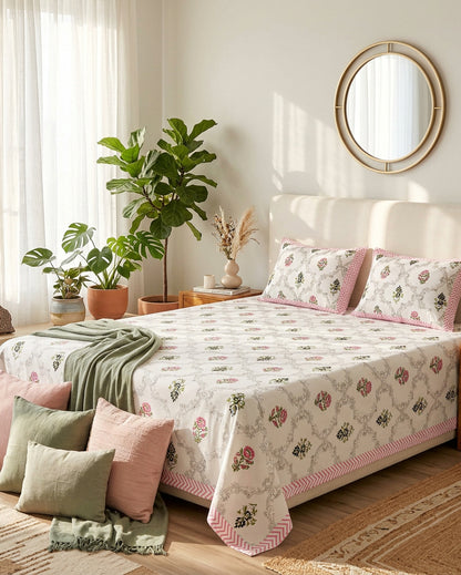 Chameli Pink bedsheet, grey trellis jaal on white with pink bloom booti, on a bed with a cream headboard with sage and pink cushions