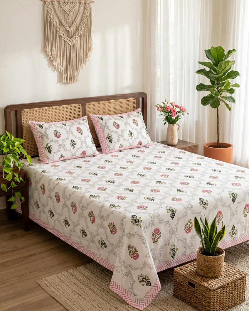 Chameli Pink bedsheet, grey trellis jaal on white with pink bloom booti, on a bed with a cane-panel headboard with macramé