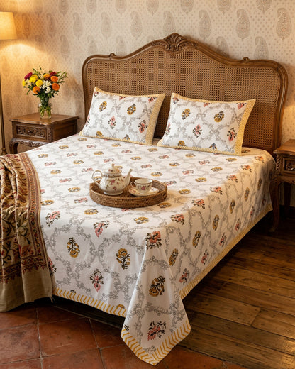 Chameli Yellow bedsheet, grey trellis jaal on white with mustard roundel bloom booti, on a bed with a cane headboard and a tea tray