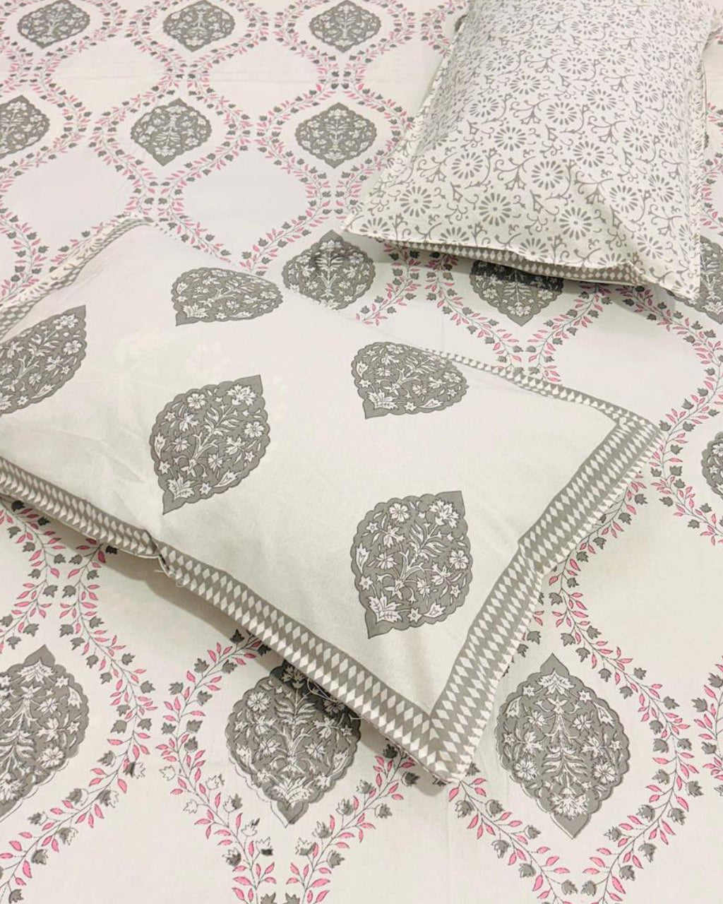 Patterned bedsheet with geometric and leaf designs on a bedspread.
