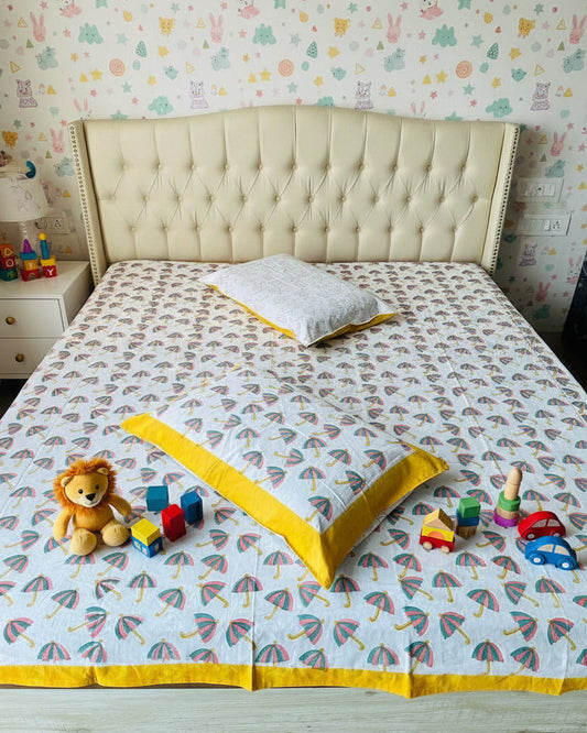 Children's bedroom with a bedspread featuring umbrella patterns and toys on a wooden floor.