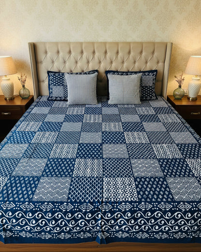 Indigo and white patchwork cotton bedsheet with striped pillow covers on an upholstered bed