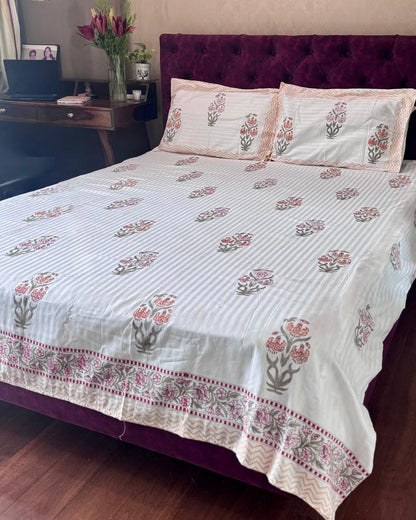 Hibiscus hand block luxe cotton bedsheet in warm tones with a saffron chevron border on a maroon velvet bed