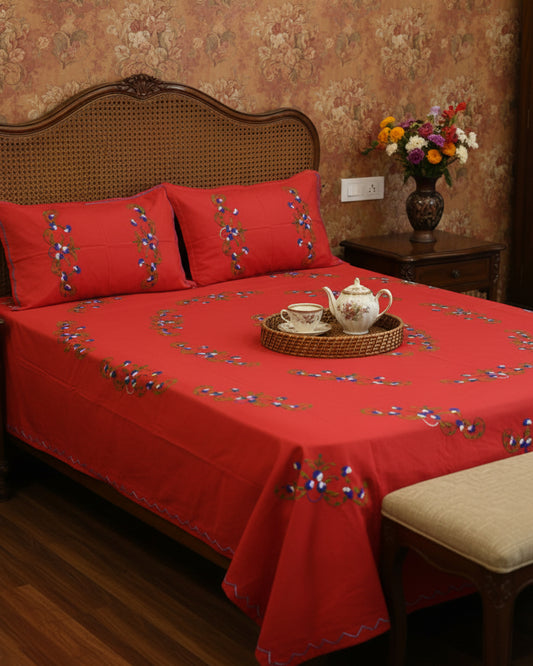 A red bedspread with matching red pillowcases decorated with colorful floral embroidery, shown on a bed in a bedroom setting.