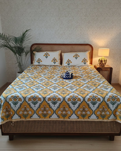 Mustard yellow and green floral cotton bedsheet on a cane bed with two matching pillow covers