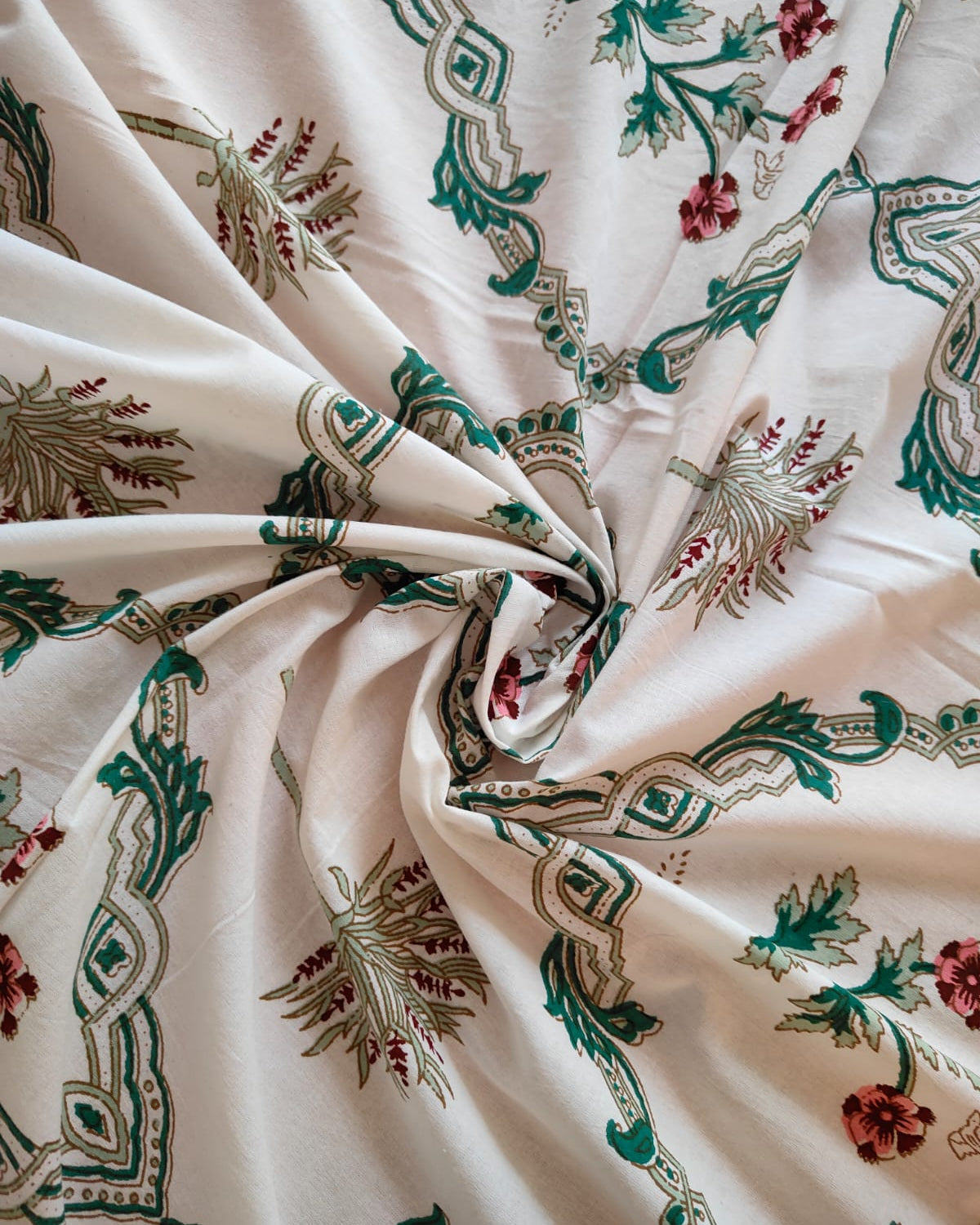 Close-up of patterned fabric with green and red designs on a white background