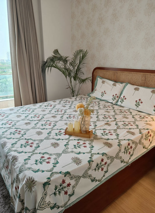 Bed with floral patterned bedsheet and wooden headboard in a room with curtains and plant.