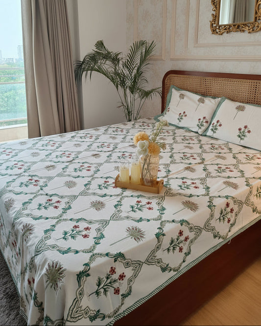 Bed with floral patterned bedsheet and wooden headboard in a room with curtains and plant.