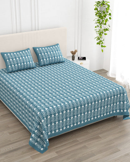 Harsingar Blue bedsheet, muted teal-blue ground with rows of white flowering stems, in a studio shot against a cream headboard
