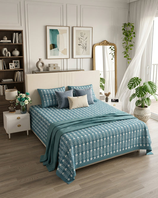 Harsingar Blue bedsheet, muted teal-blue ground with rows of white flowering stems, in a bedroom with a teal throw and cushions