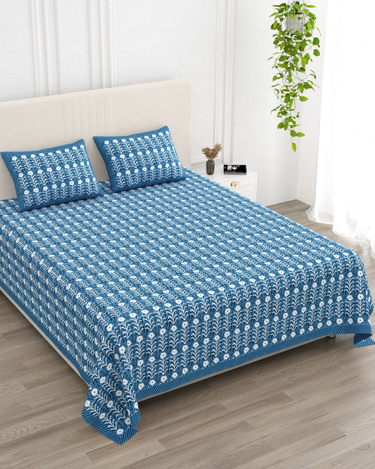 Harsingar Dark Blue bedsheet, cobalt-blue ground with rows of white flowering stems, in a studio shot against a cream headboard