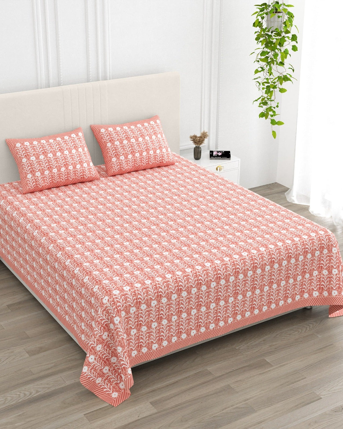 Harsingar Pink bedsheet, coral-pink ground with rows of white flowering stems, in a studio shot against a cream headboard