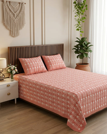 Harsingar Pink bedsheet, coral-pink ground with rows of white flowering stems, on a bed with a slatted wood headboard with macramé