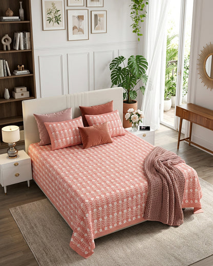 Harsingar Pink bedsheet, coral-pink ground with rows of white flowering stems, in a bedroom with rose cushions and a knit throw