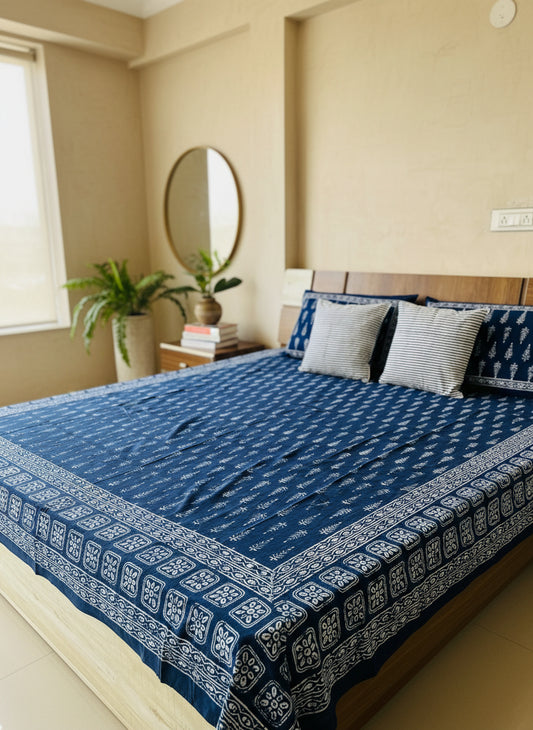 Bed with blue and white patterned bedspread and pillows against a beige wall.