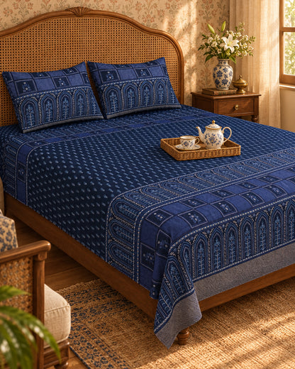 Tarang Blue navy bedsheet with arched border and a tea tray on a cane-headboard bed