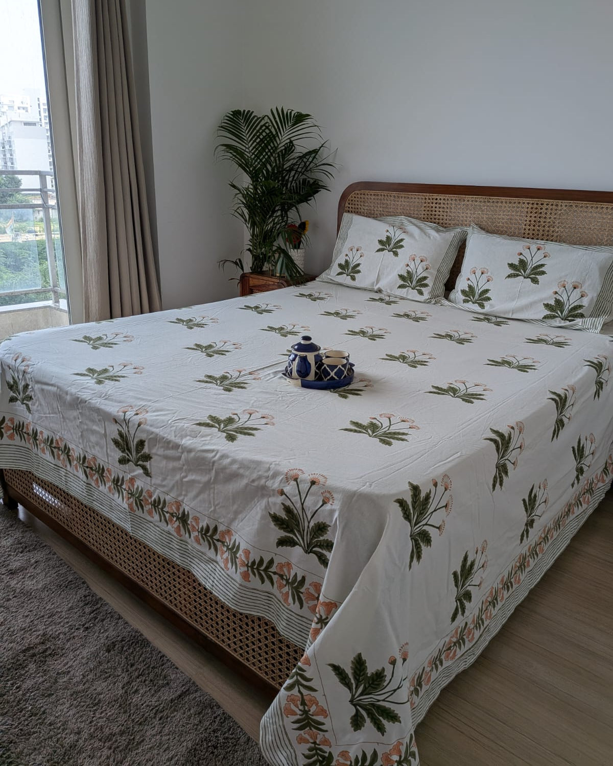 White jasmine hand block cotton bedsheet with olive green stems on a cane headboard bed
