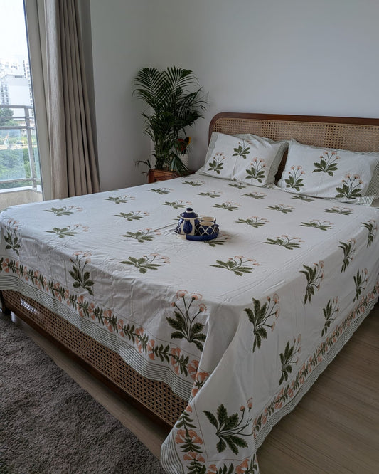 White jasmine hand block cotton bedsheet with olive green stems on a cane headboard bed