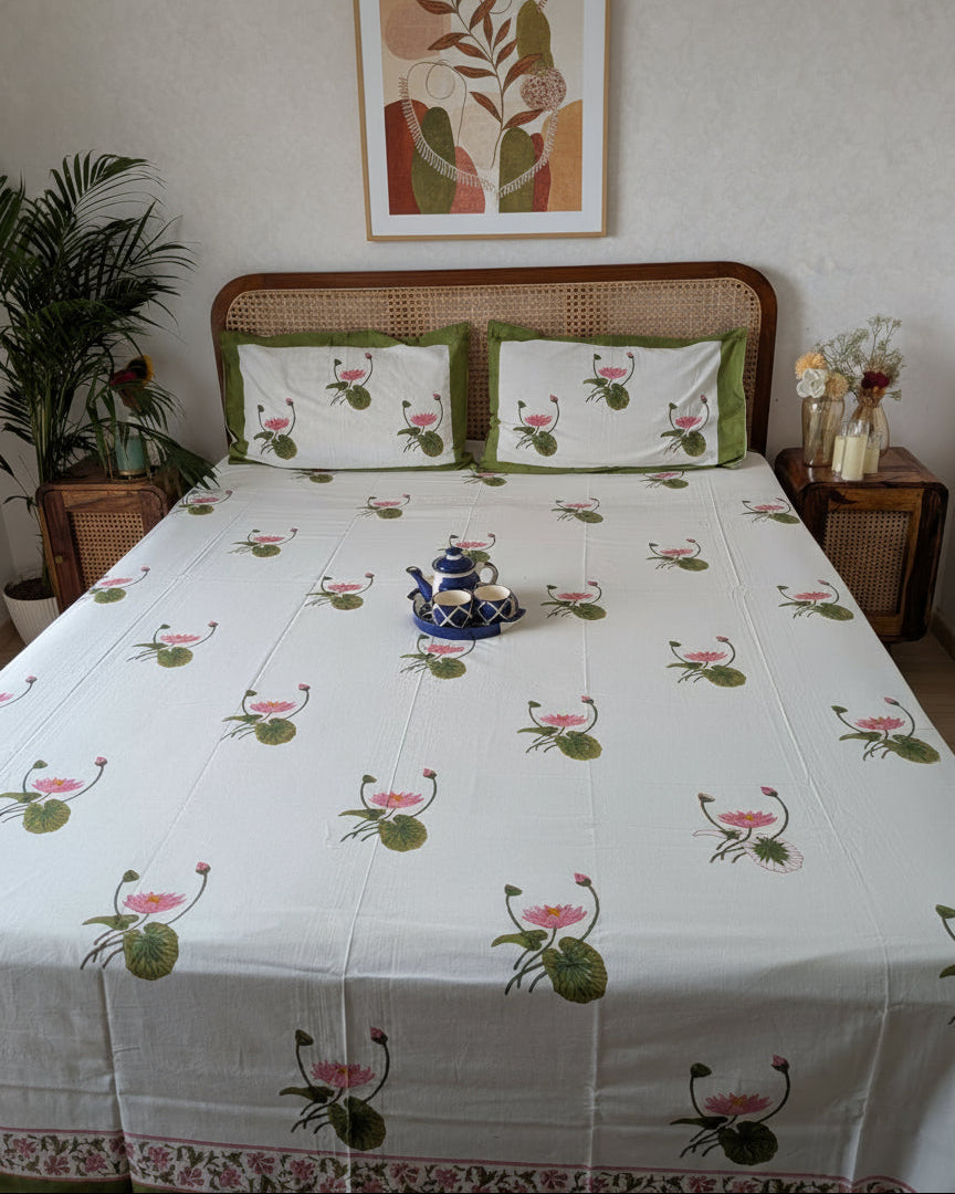 Bed with floral patterned bedsheet and pillows with lotus motif in a room setting.